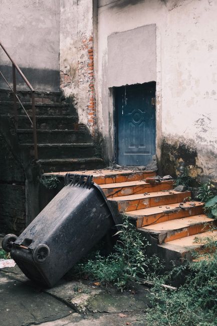A straight flight of industrial stairs with yellow safety risers and black anti-slip treads, situated within a warehouse or factory environment. The staircase is flanked by metal handrails painted yel